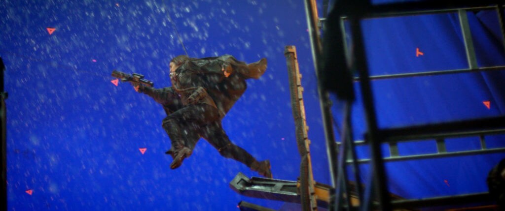 A performer in a wire rig leaps in front of a blue screen, on the set of Rogue One.