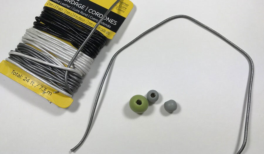 A gray leather cord next to three painted beads.