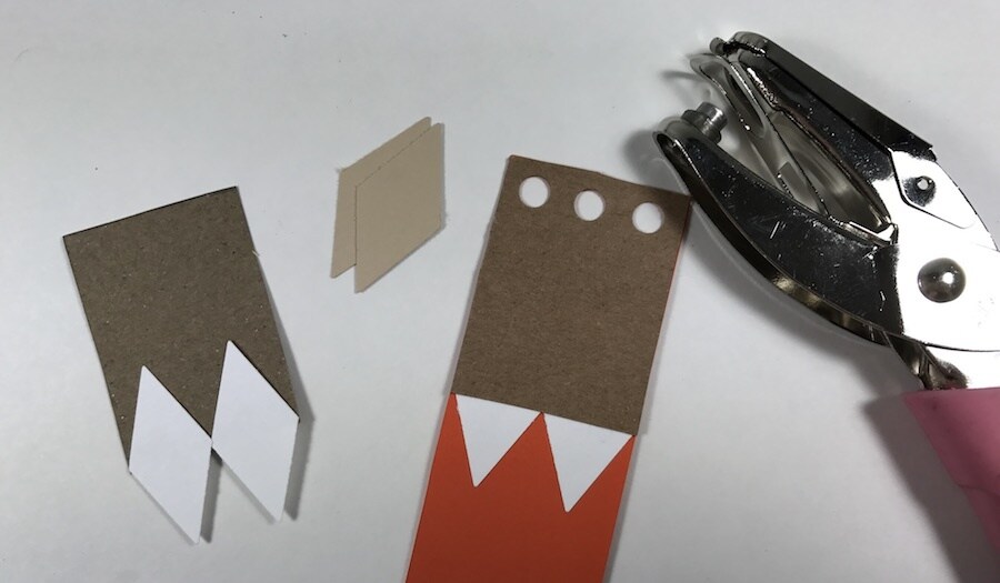 A partly assembled cardboard bookmark beside a hole punch.