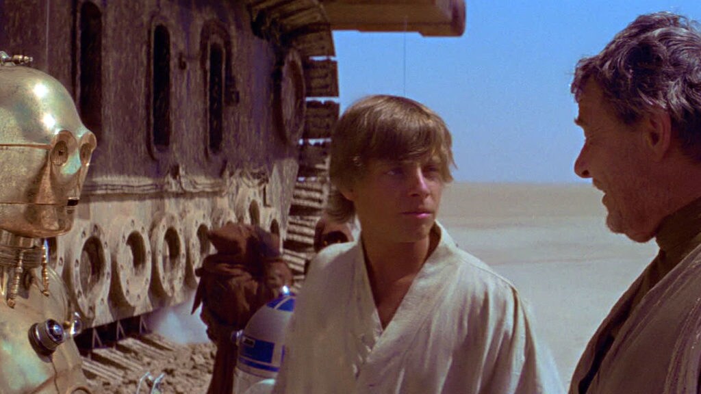 Luke talks to his uncle Owen with C-3PO standing next them and R2-D2 and Jawas in the background in front of a sandcrawler in A New Hope.