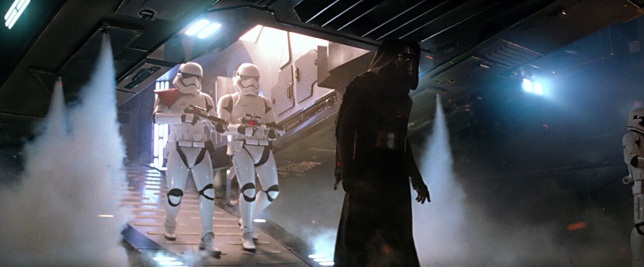 Kylo Ren disembarks from his ship with two stormtroopers following behind.