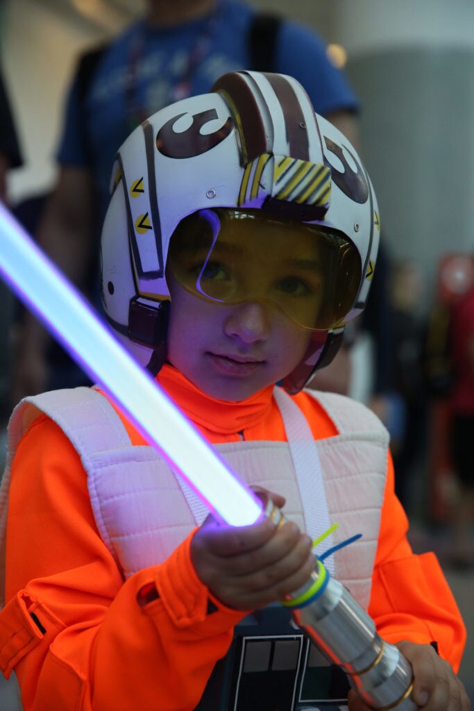 A child cosplays as a Rebel fighter holding a lightsaber at Star Wars Celebration.