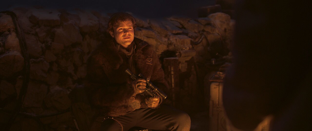 Han sits at a campfire holding a blaster pistol in Solo: A Star Wars Story.