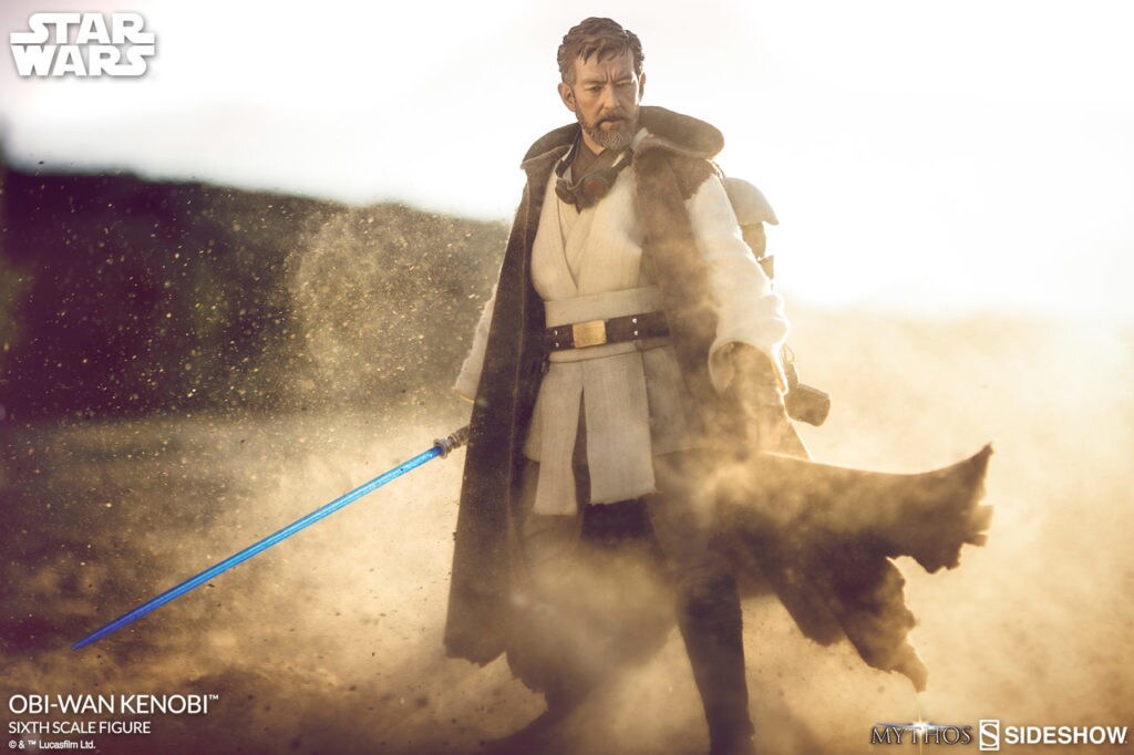 The Star Wars Mythos Obi-Wan Kenobi action figure grasps his lightsaber in a dusty, sunny setting.