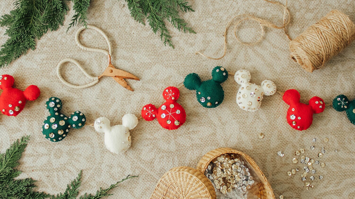 A holiday garland of many off-white, green, and red felt Mickey Mouse heads decorated with beads and sequins.