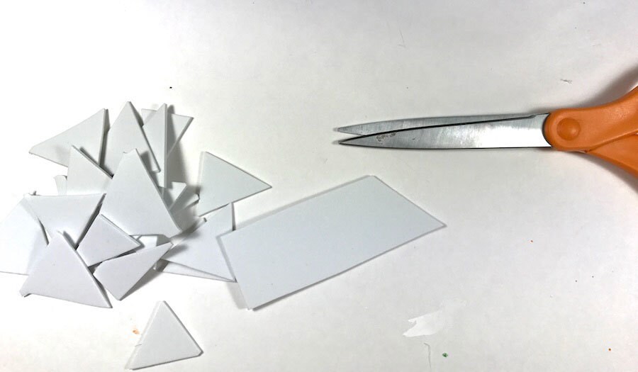 A stack of white craft paper triangles next to a pair of scissors.