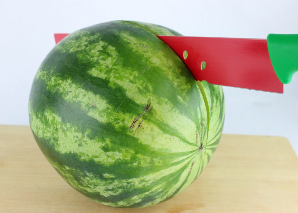 A watermelon with a red-bladed knife slicing through it in preparation for making Rebel Alliance Chili-Lime Melon Pops.