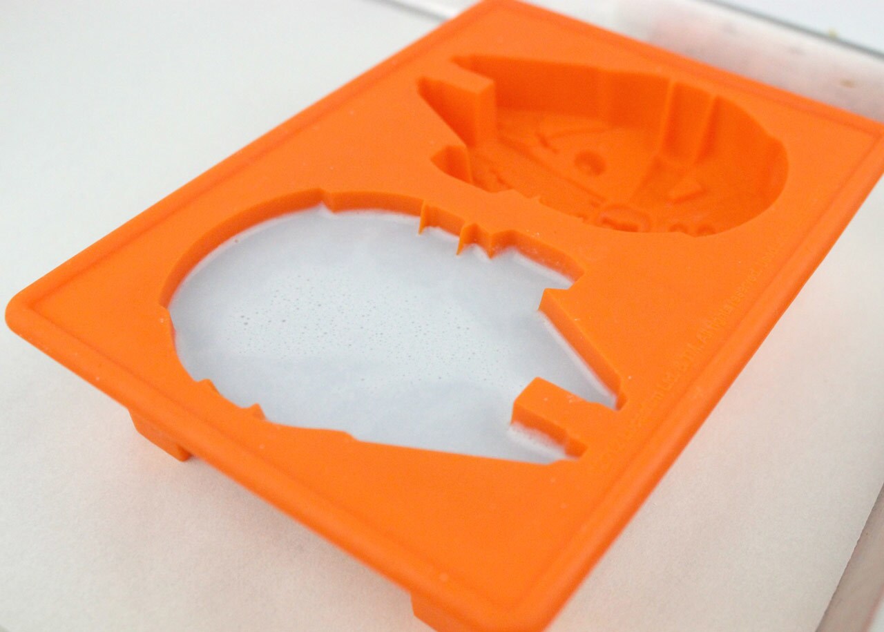 An orange-colored Millennium Falcon ice cream mold filled with an ice cream base is prepared for freezing.