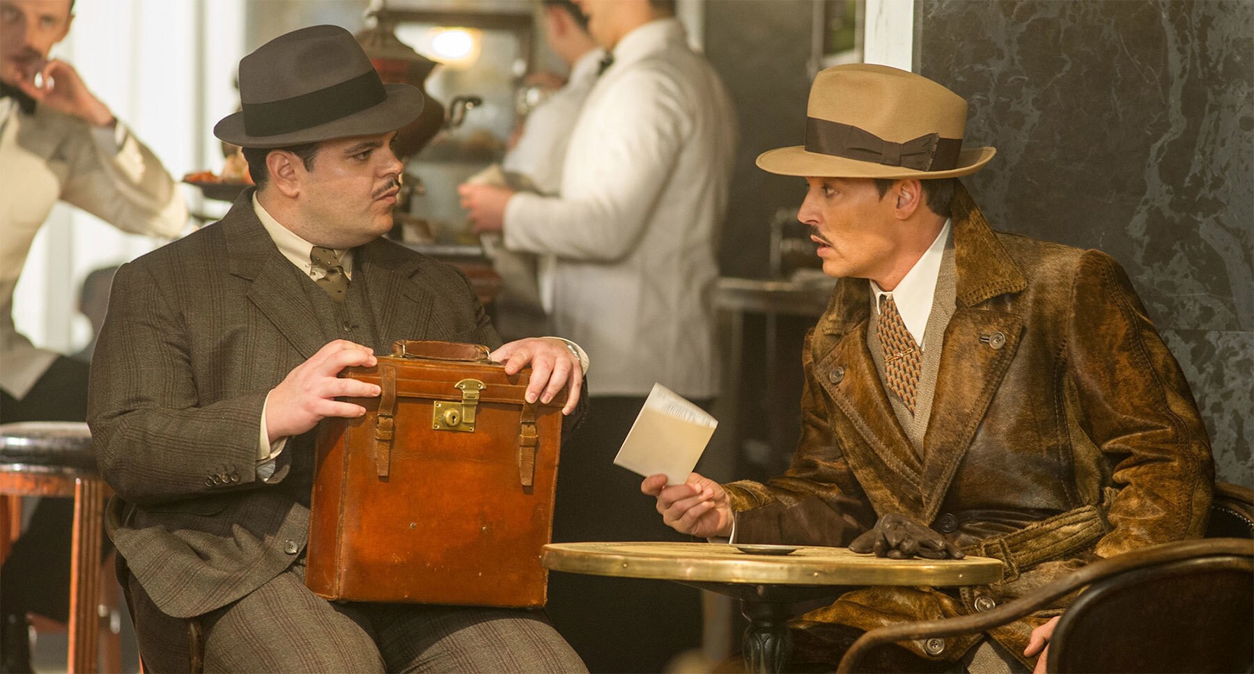 Johnny Depp (as Edward Ratchett) and Josh Gad (as Hector MacQueen) sitting at a table in "Murder on the Orient Express"