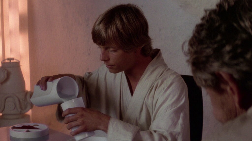 Luke sits at a table pouring blue milk into a cup in A New Hope.