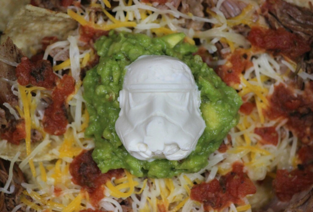 A fully loaded plate of nachos with sour cream in the shape of a stormtrooper's head.
