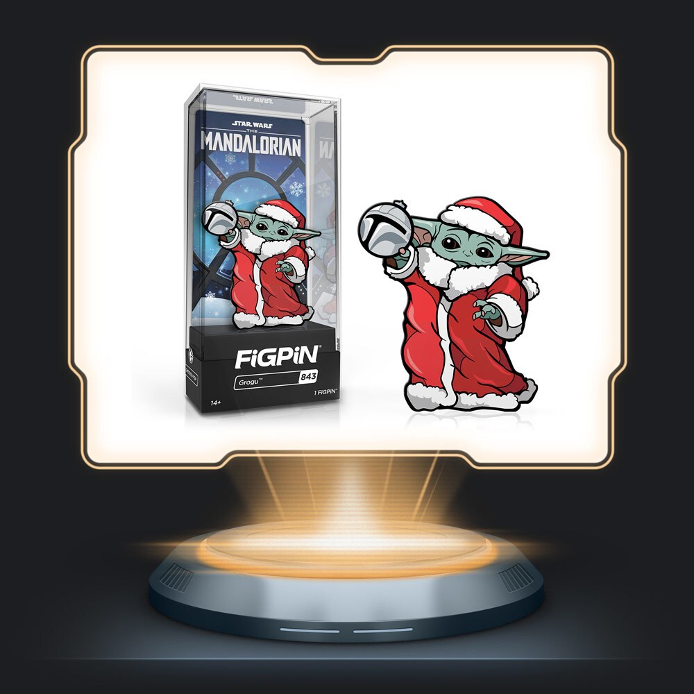 Holiday Grogu by FiGPiN featuring Grogu in a Santa outfit hanging a Mandalorian ornament.
