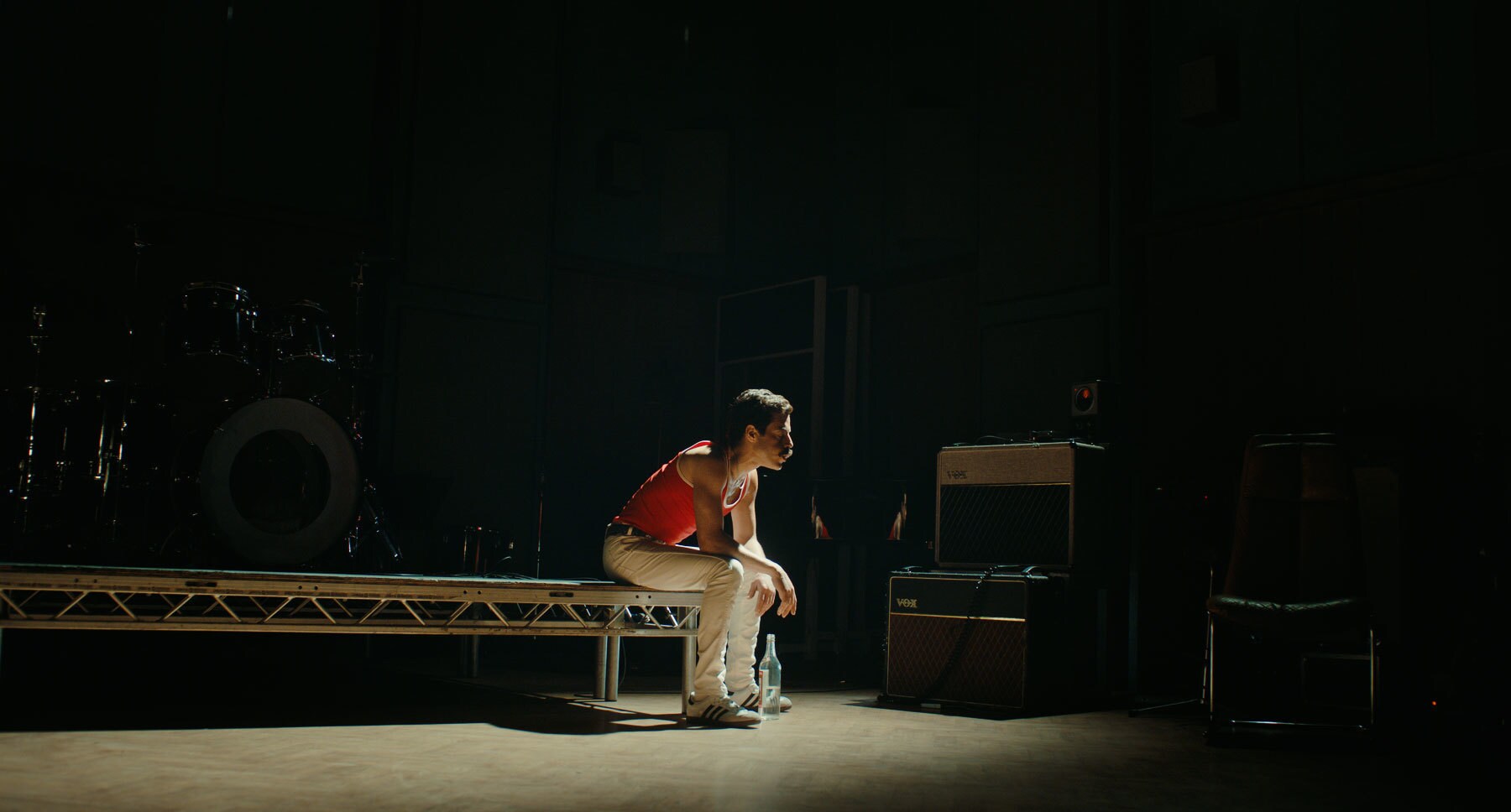  Actor Rami Malek (as Freddie Mercury) sitting on the edge of a stage in the movie "Bohemian Rhapsody"