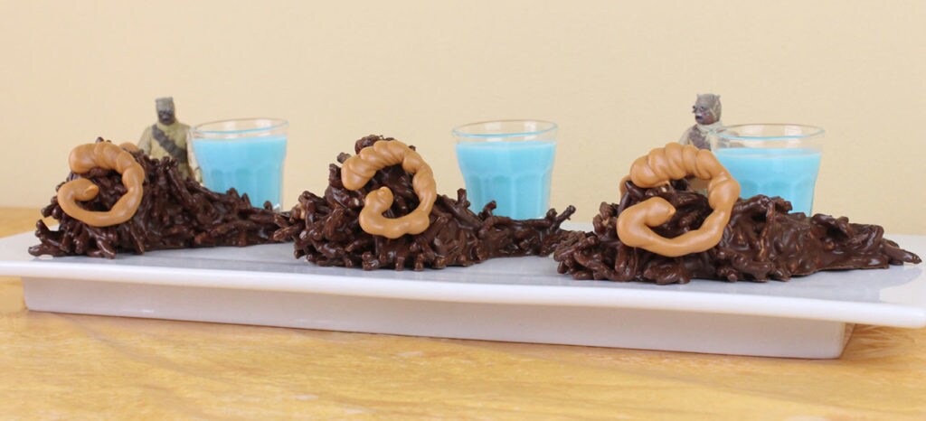 Three Bantha Bites on a plate with three glasses of blue milk and two Tusken Raider action figures.