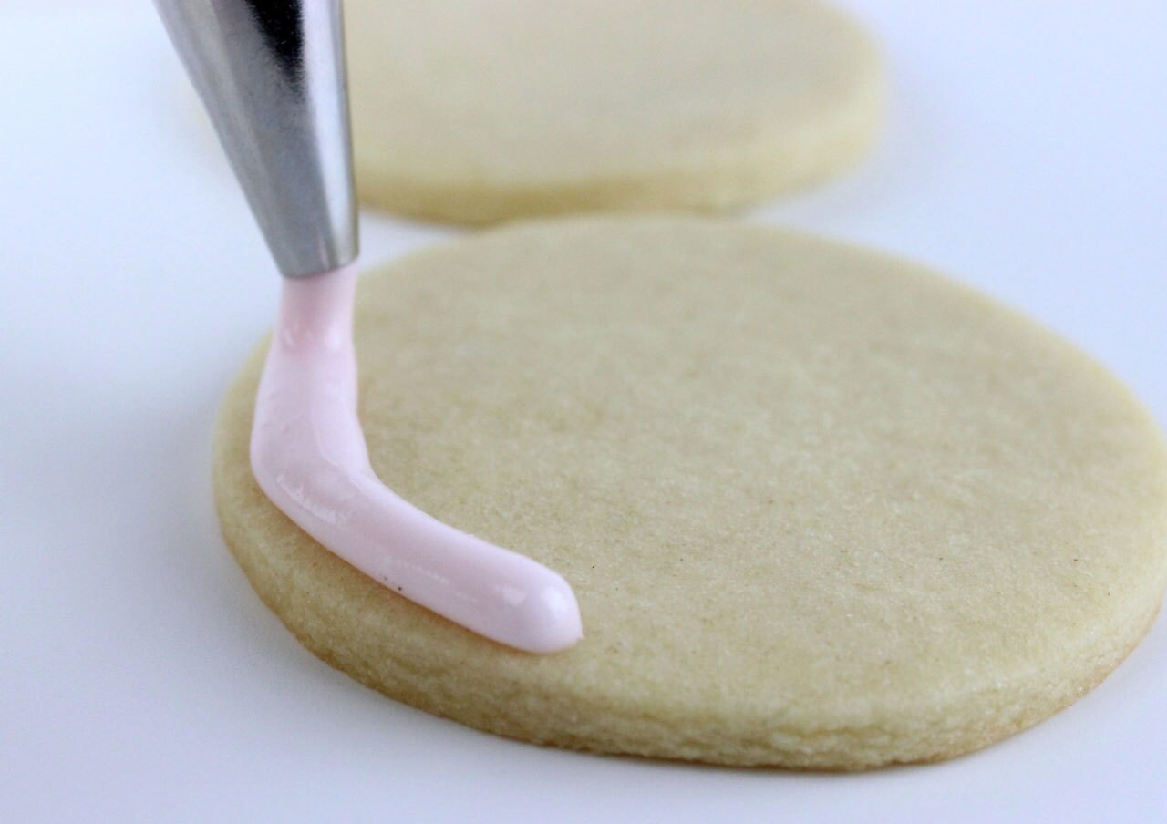Pink icing is piped onto a cookie.