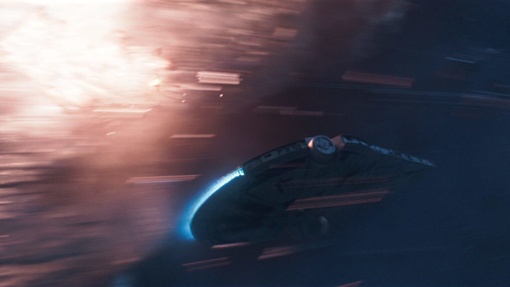 The Millennium Falcon speeds through the galaxy as a TIE fighter explodes behind it in Solo: A Star Wars Story.