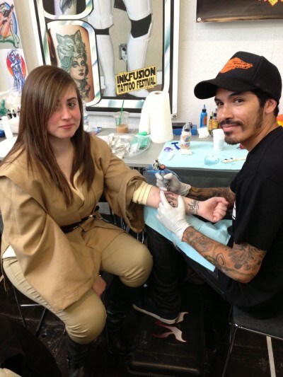 A tattoo artist gives a fan dressed as a Jedi a tattoo on her inner forearm at Star Wars Celebration Europe.
