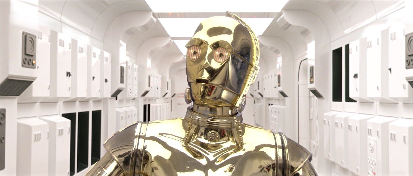 C-3PO walks down a hallway of the consular ship Tantive IV.