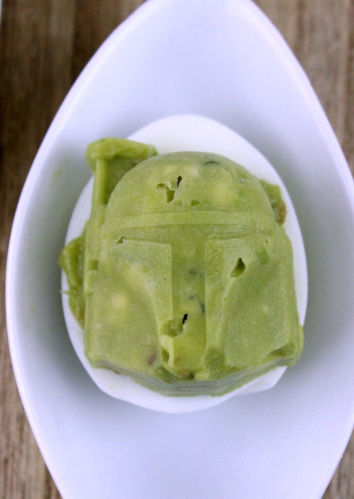 Boba Fett in his Mandalorian armor, formed from a silicon mold of guacamole, sits on top of a hard boiled egg half.