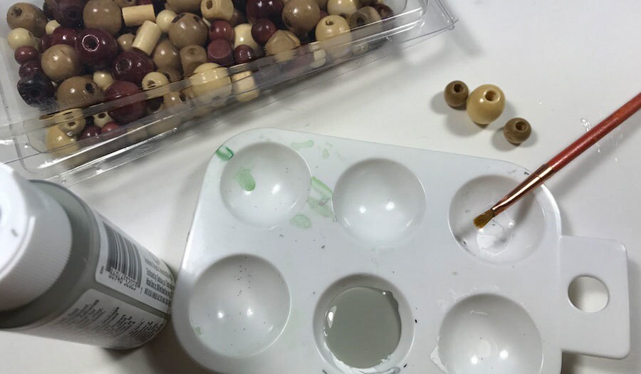 Paint, a paintbrush, and a box of beads on a table. Gray paint has been poured into a paint tray.