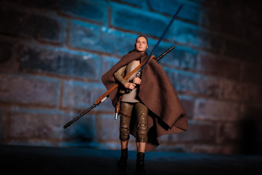 A Rey action figure from the Star Wars: The Black Series collection. She wears a brown cloak and carries a bow and lightsaber.