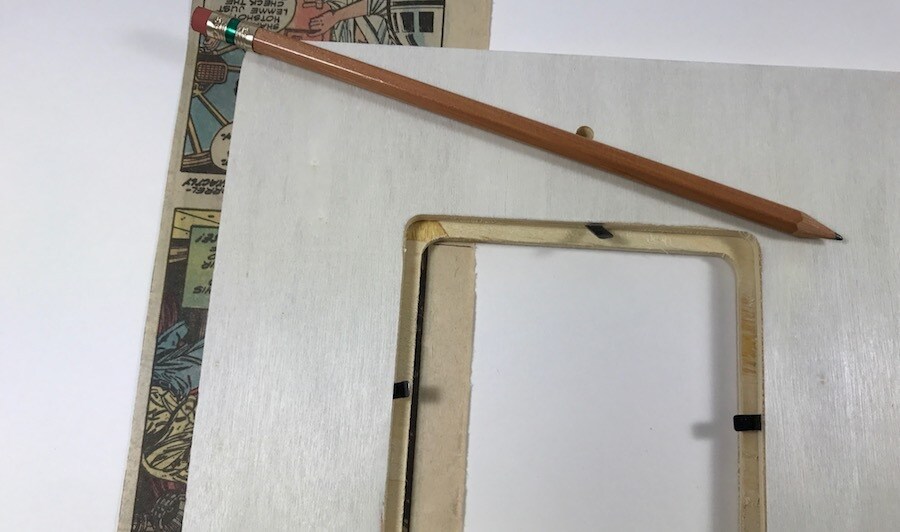 A wooden picture frame, a pencil, and a page torn from a comic book.