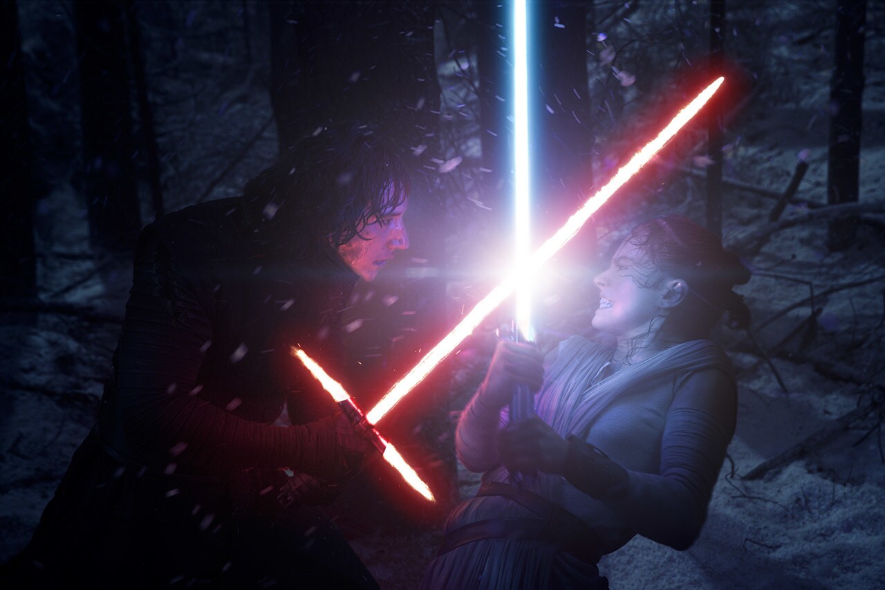 Kylo Ren crosses lightsabers with Rey in a dark forest.