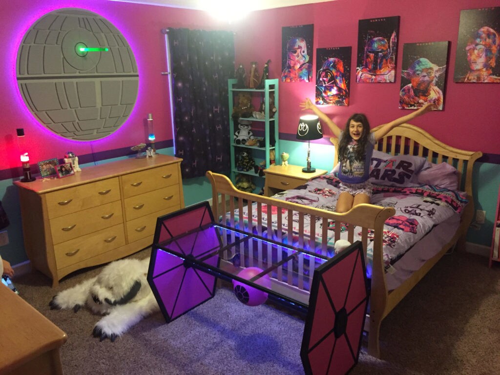 Star Wars super-fan Emmie kneels on her Star Wars themed bed. Her room is decorated in Pink and has Imperial themed decor.