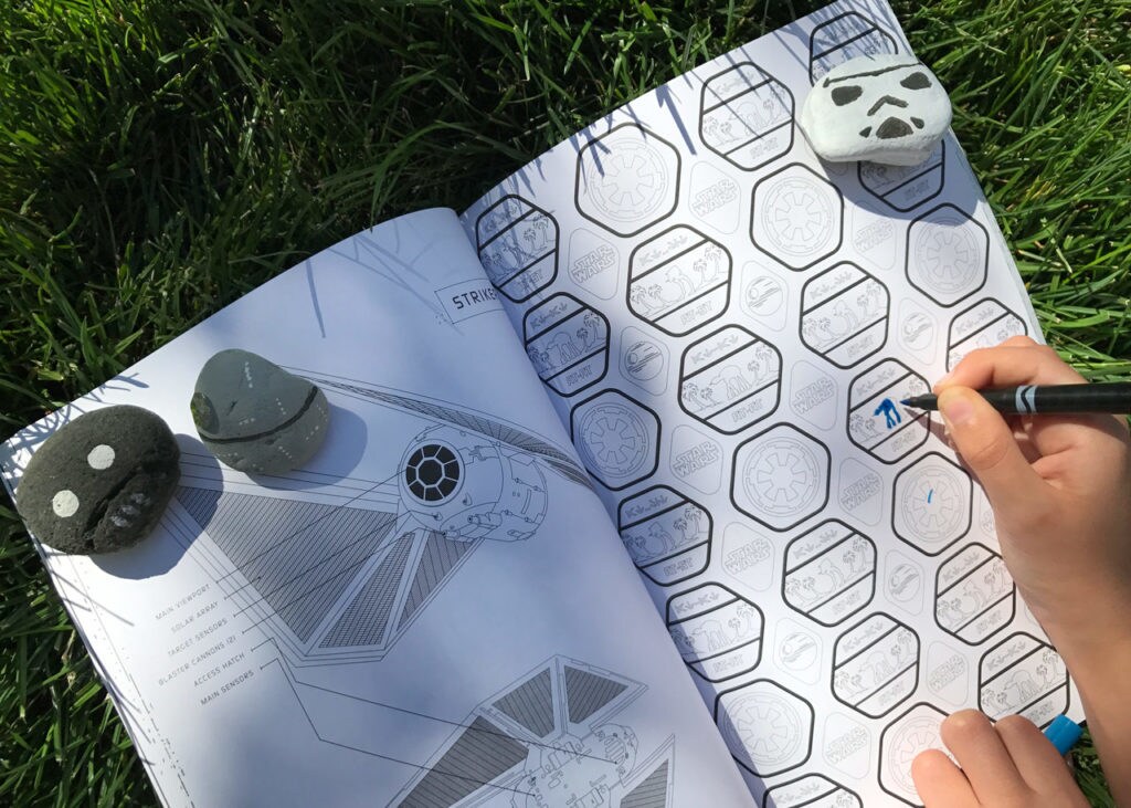A child plays in a Star Wars themed coloring book held open by stones decorated as a Stormtrooper, the Death Star, and K-2SO.