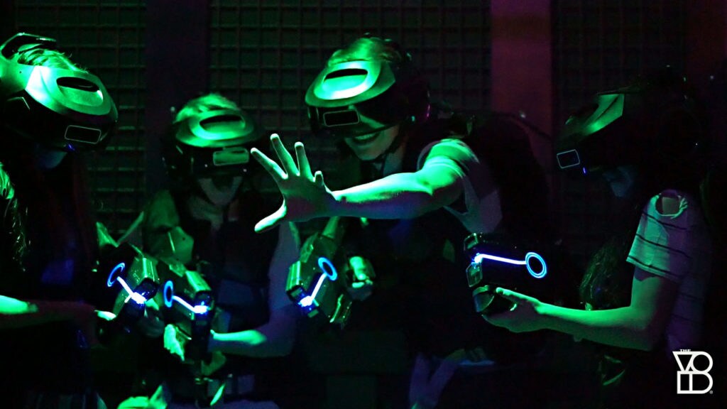 Four people equipped with VR helmets and blasters enjoy themselves.