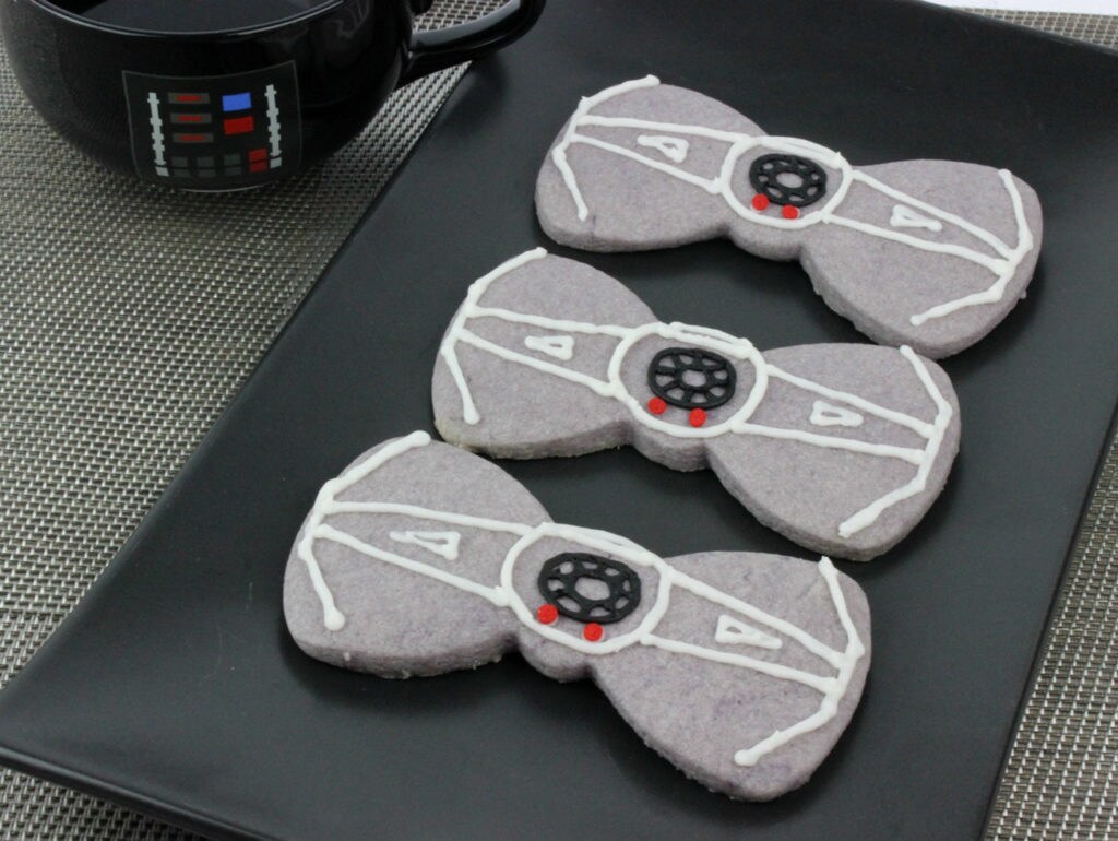 A plate of bowtie shaped cookies decorated to look like TIE fighters.
