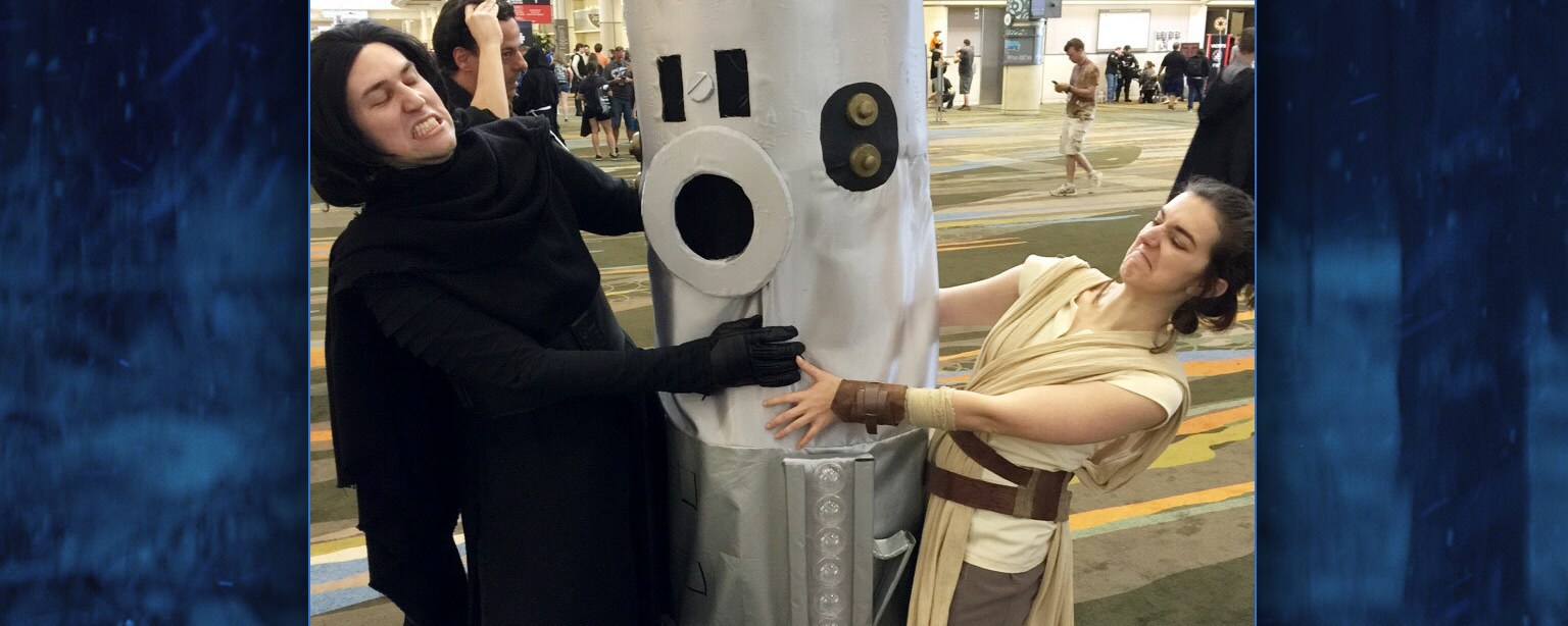 Cosplayers of Kylo Ren and Rey fight over a cosplayer dressed as a lightsaber.