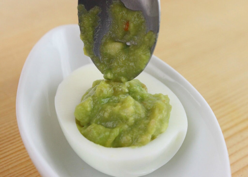 Guacamole is spooned into a hard boiled egg half.