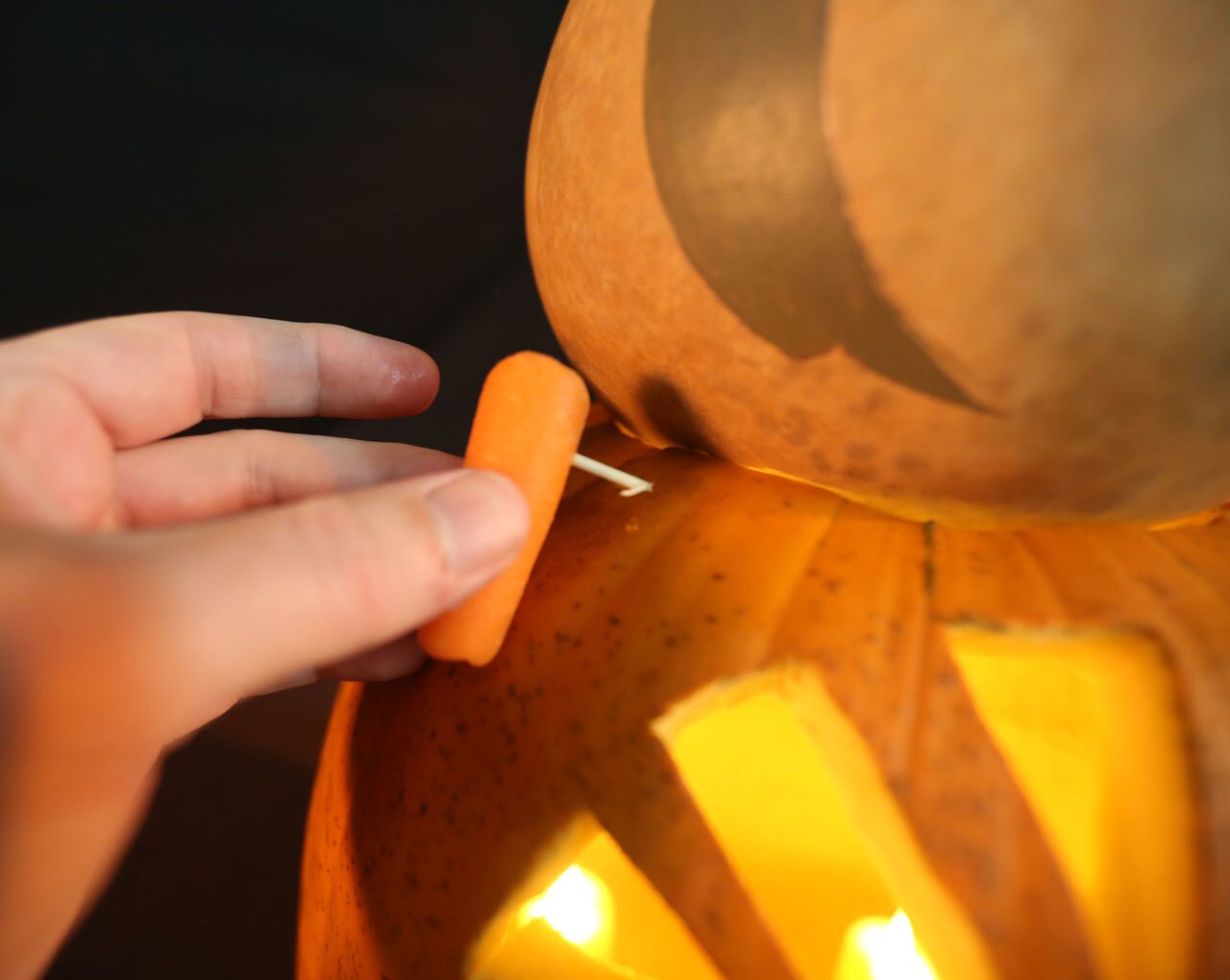 Using baby toothpicks, a person places carrots between the Chewbacca pumpkin on the bottom and the porg gourd on top. The carrots will serve as the porgs feet.
