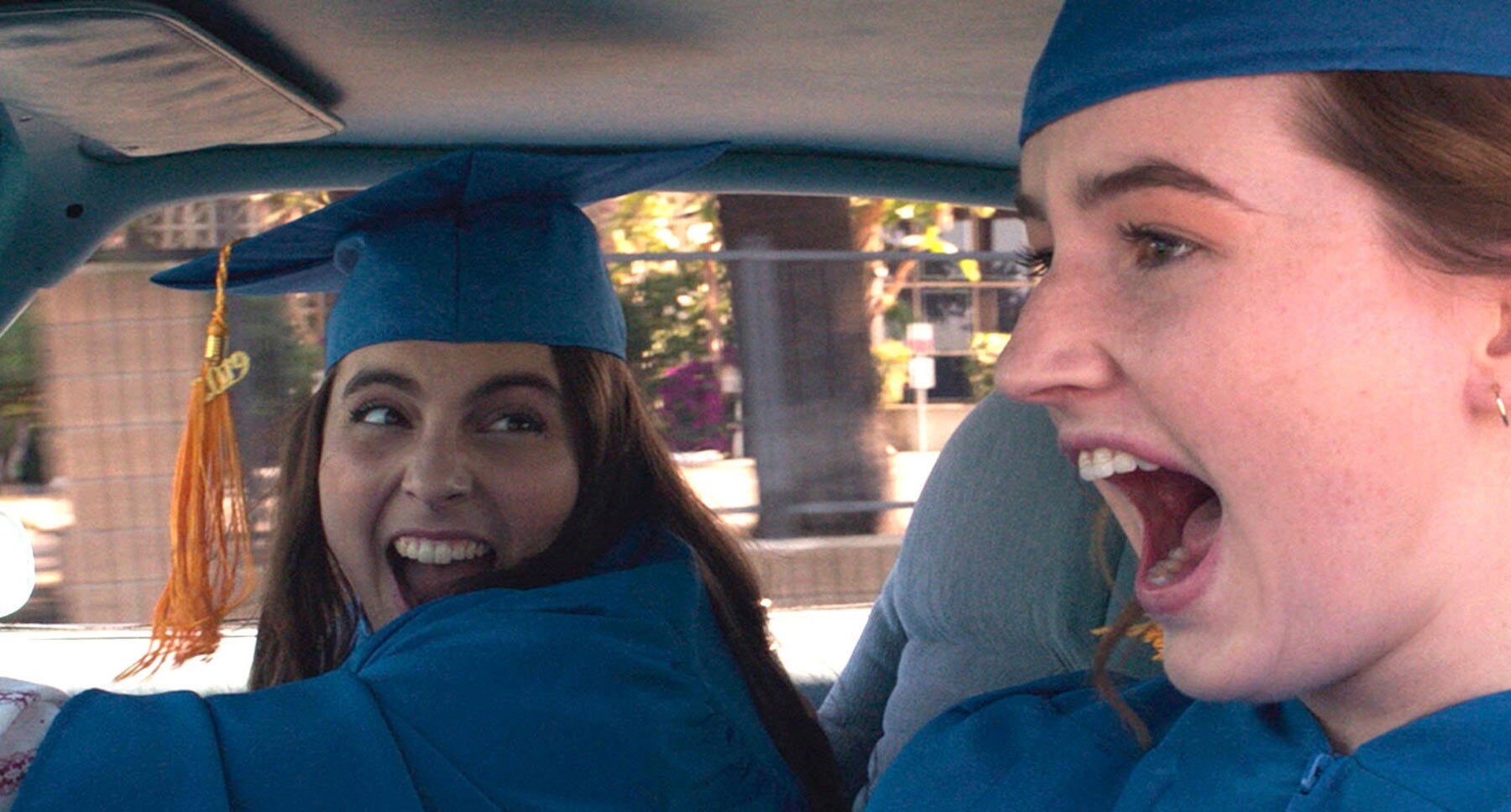 Actors Kaitlyn Dever (as Amy) and Beanie Feldstein	(as Molly) screaming in a car wearing cap and gown in the movie "Booksmart"