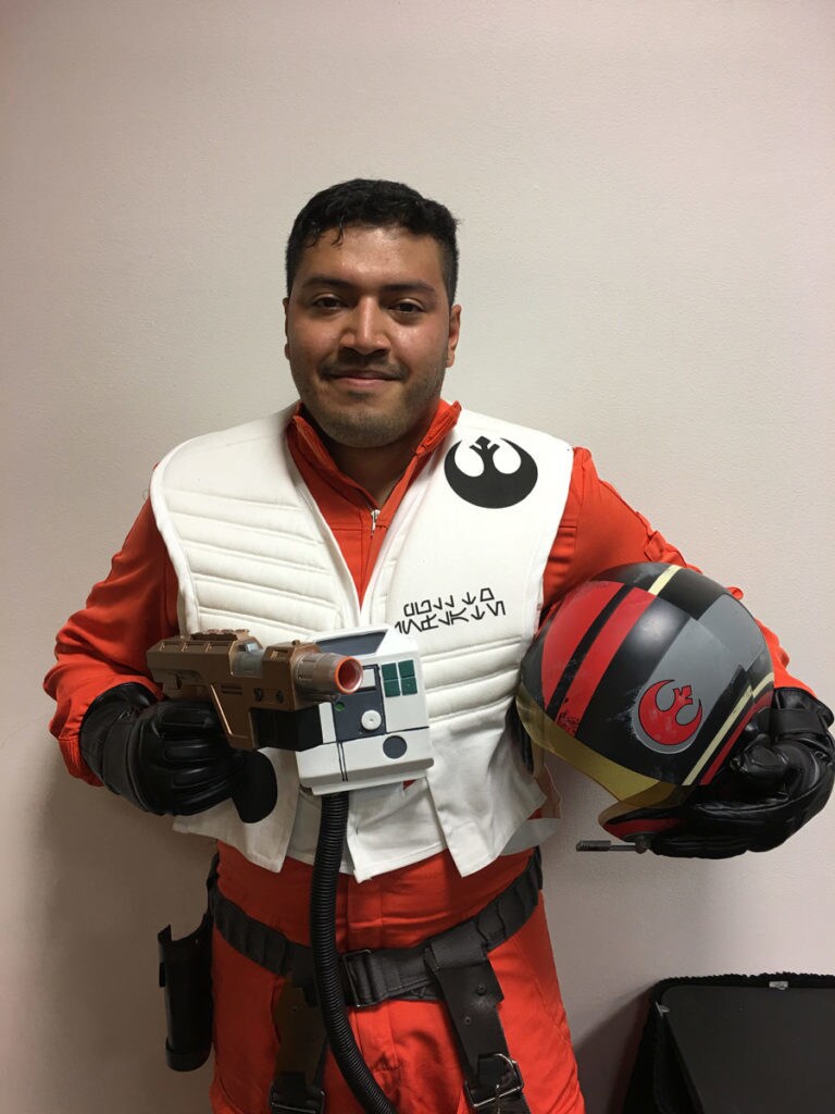 Cosplayer David Lopez, dressed as Poe Dameron, holds a blaster made from a nerf gun and a helmet.