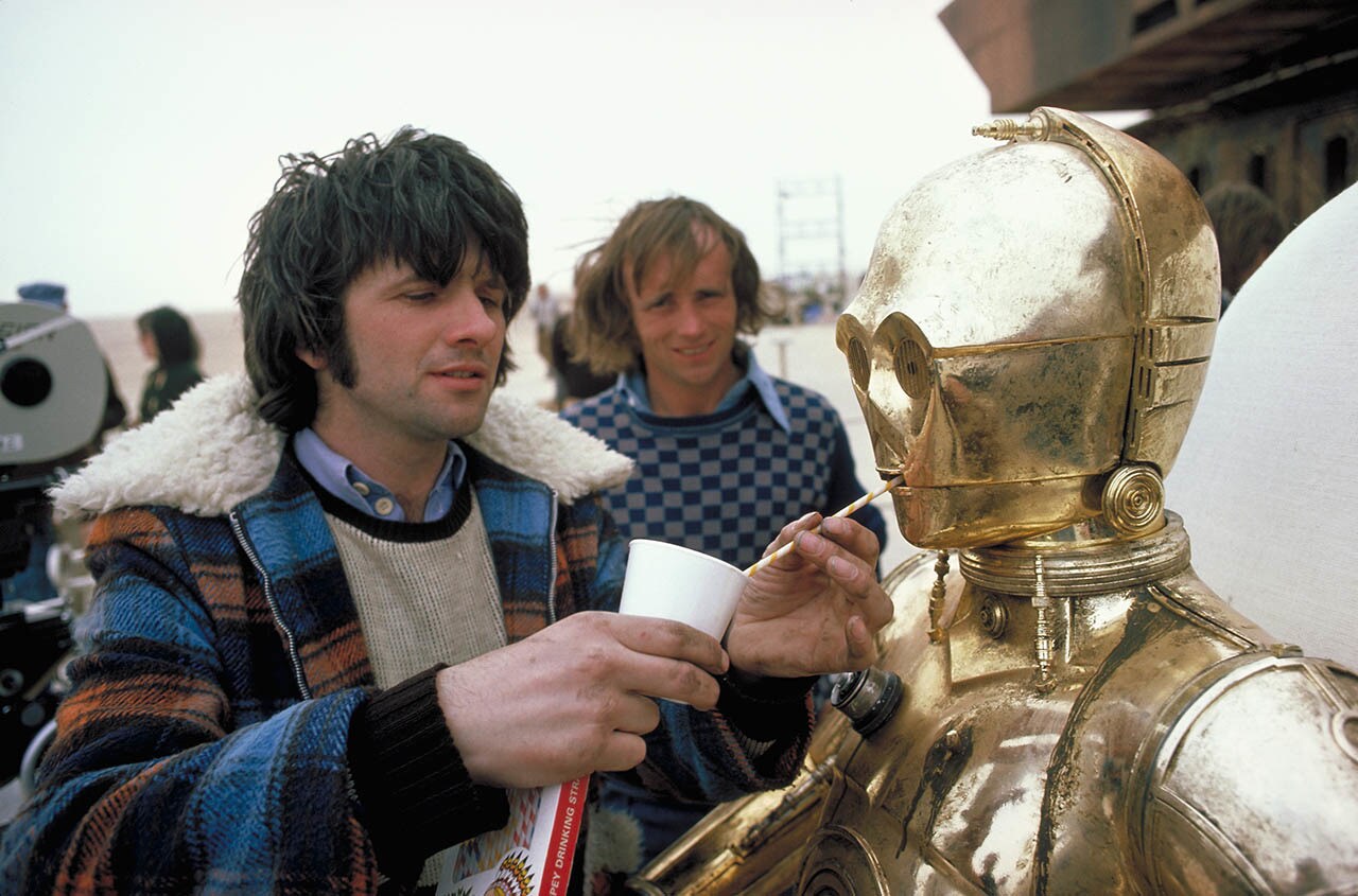Anthony Daniels as C-3PO is helped with a drink on the set of Tatooine.
