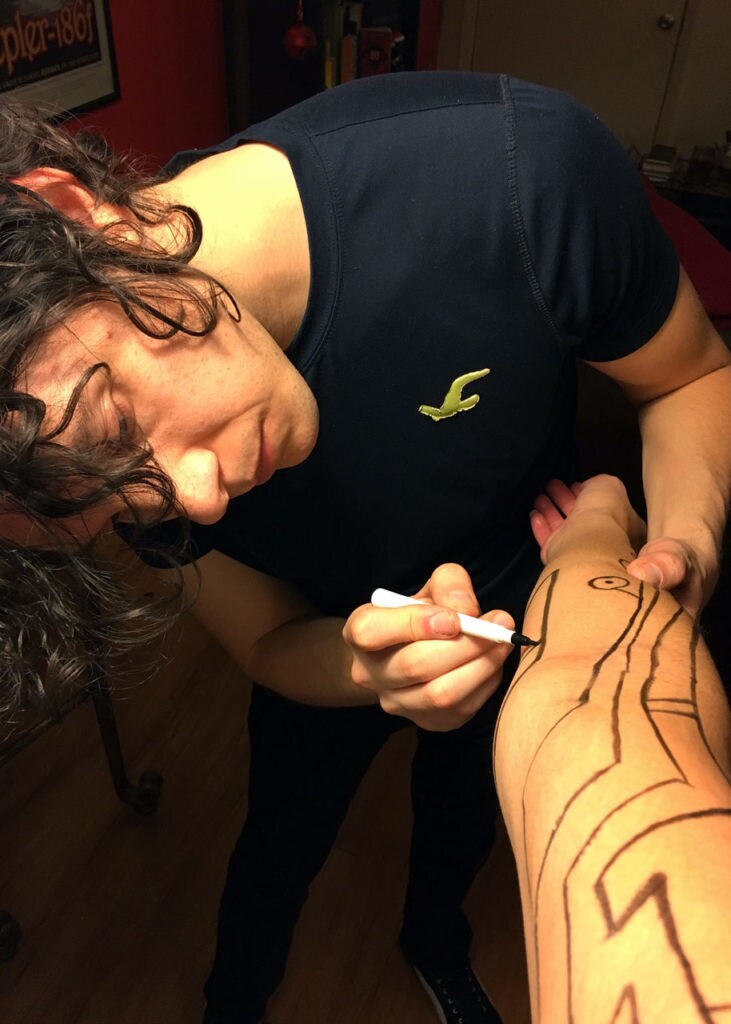 Cosplayer Alyssa Vidales's boyfriend draws part of her costume on her arm.