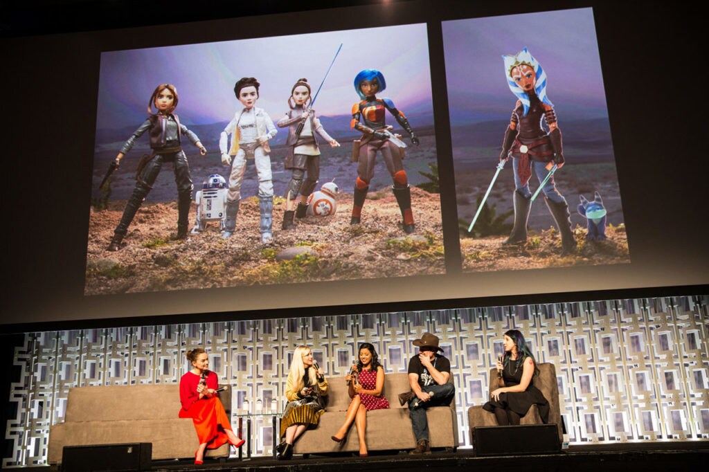 Ashley Eckstein, Tiya Sircar, Dave Filoni, and Daisy Ridley are interviewed by host and author Amy Ratcliffe while a giant screen above them shows various female heroines of the Star Wars universe at Star Wars Celebration Orlando.