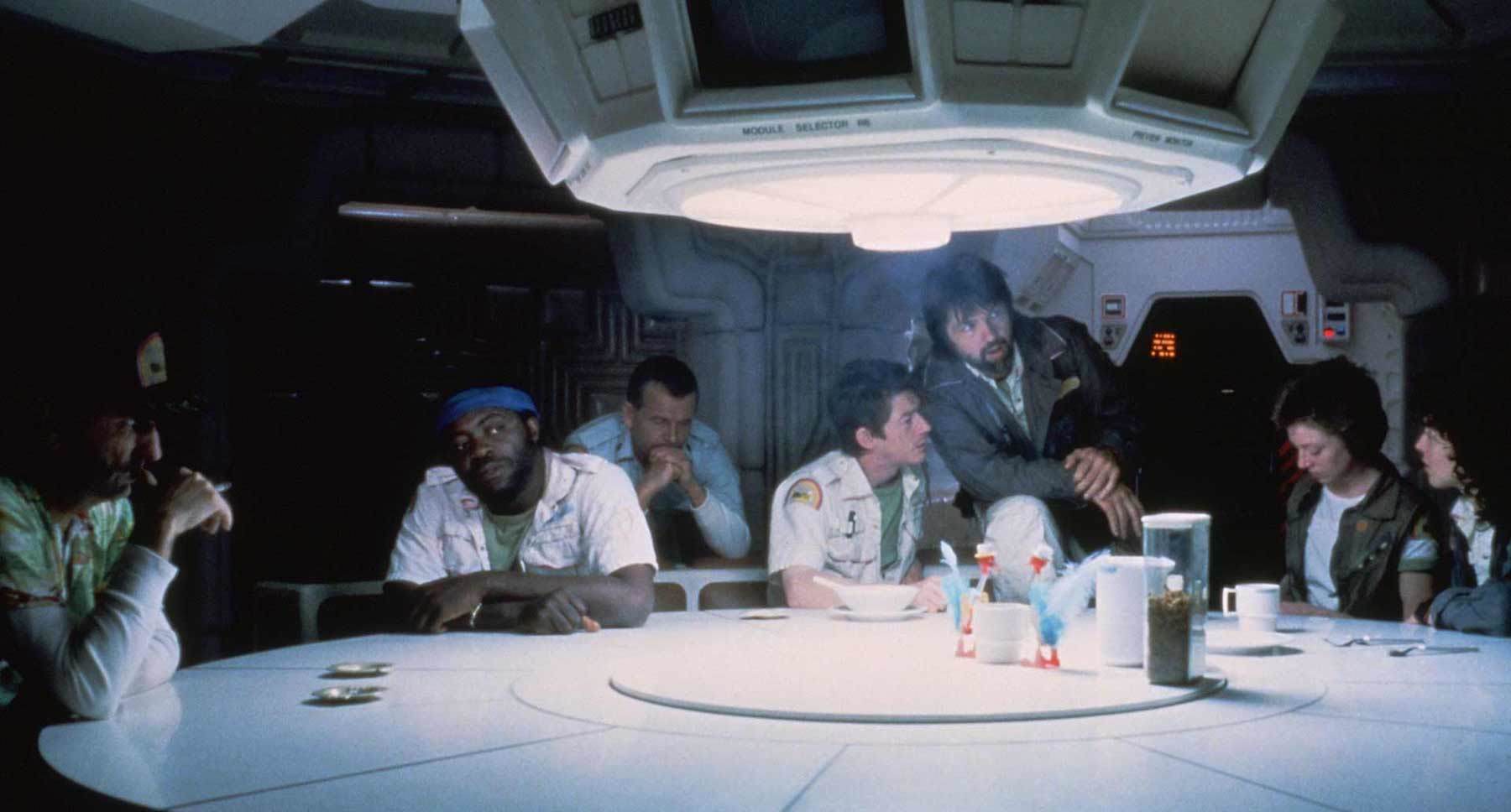 Dallas (actor Tom Skerritt), Ripley (actor Sigourney Weaver), Lambert (actor Veronica Cartwright), Brett (actor Harry Dean Stanton), Kane (actor John Hurt), Ash (actor Ian Holm), and Parker (actor Yaphet Kotto) at a table in the movie "Alien."