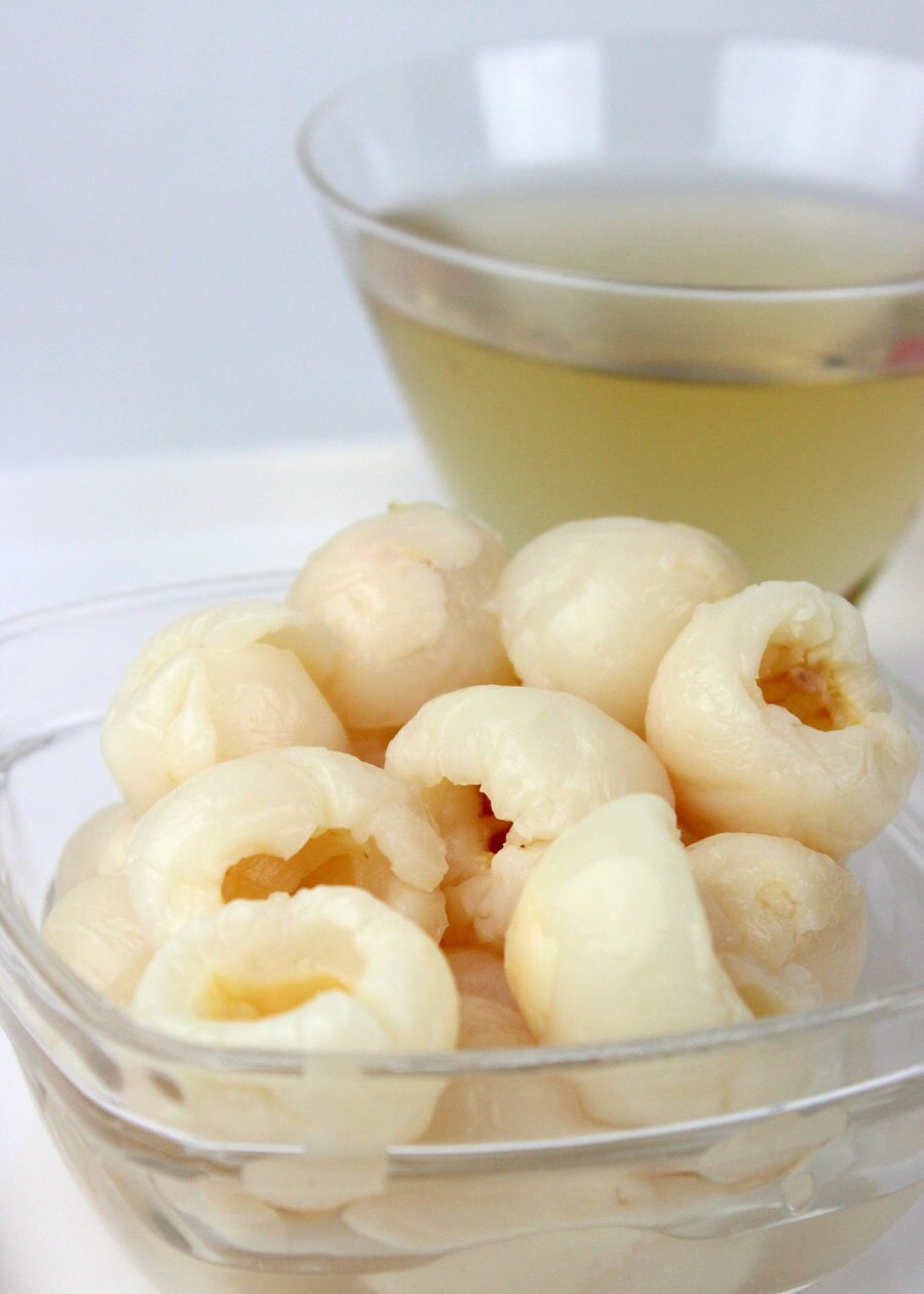 A bowl of peeled lychee fruits next to a glass of juice.