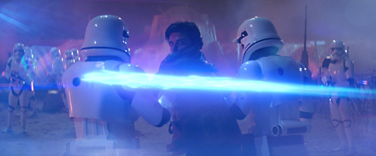 Two stormtroopers take Poe Dameron into custody on Jakku while other stormtroopers stand guard in The Force Awakens.