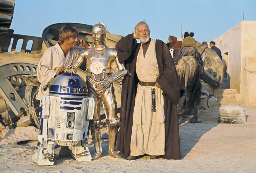 In a behind-the-scenes photo from A New Hope, Obi-Wan poses, candidly, alongside Luke Skywalker, R2-D2, and C-3PO.