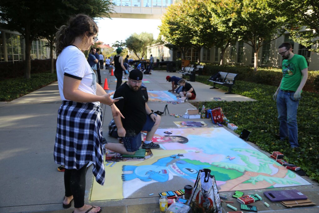 Artists from Lucasfilm and ILM work on their chalk drawings at the Lucasfilm Sidewalk Art Festival in San Francisco. In the foreground, an artist kneels in front of his team's drawing that features Lilo and Stich.