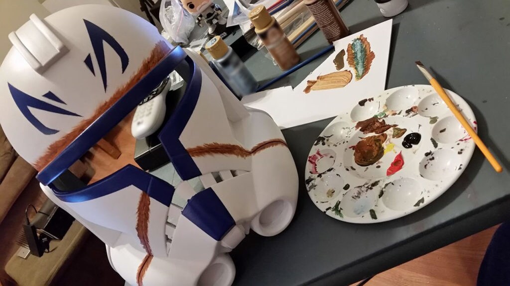 A costume stormtrooper helmet modeled after Captain Rex's armor on a crafting table with paints.