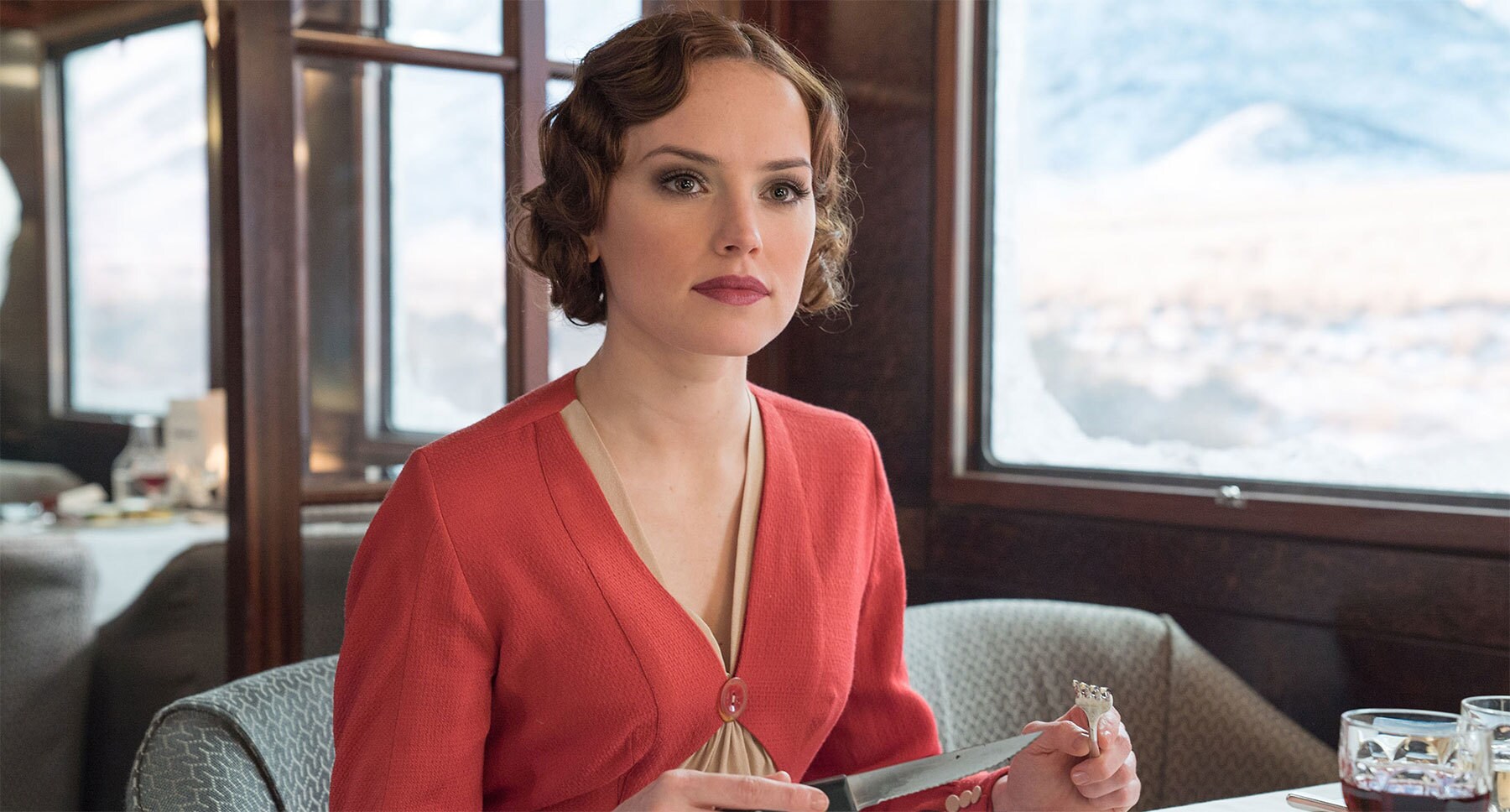 Daisy Ridley (as Mary Debenham) sitting at a dining table in "Murder on the Orient Express"