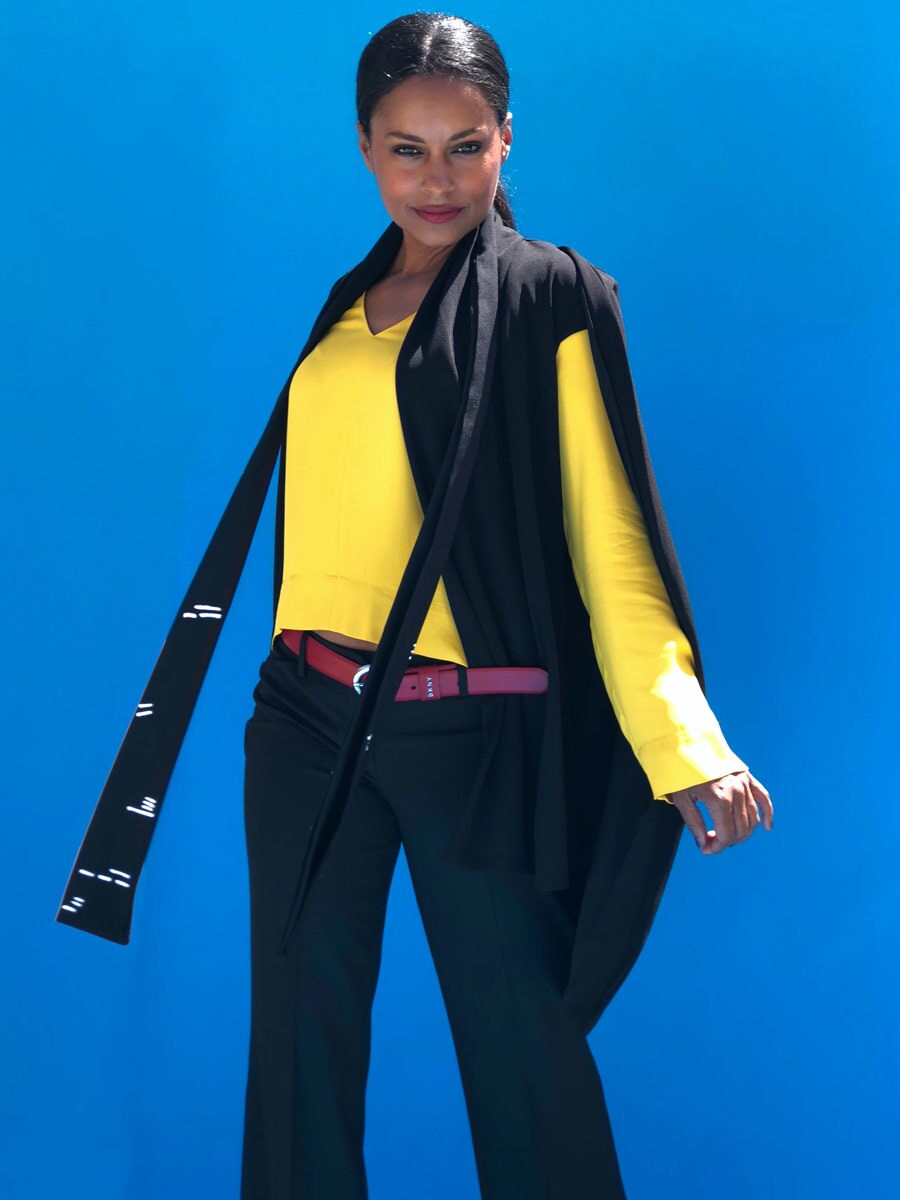 A female model dressed to look like Lando Calrissian with a yellow dress shirt, black pants, red belt, and a black cape blazer.
