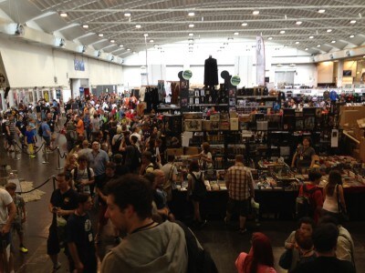 A crowded convention hall with people and merchandise booths.