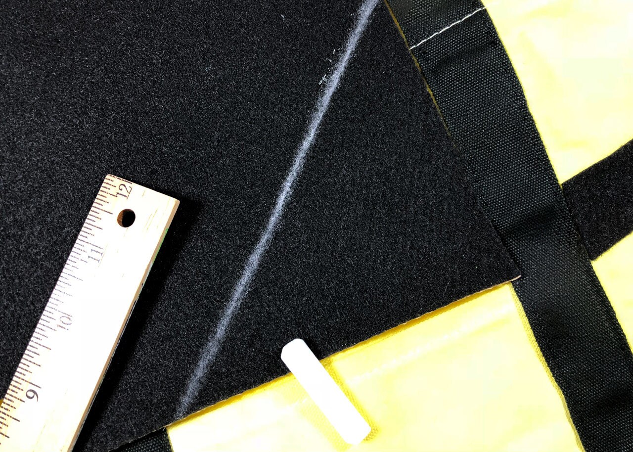A chalk line creates a triangle on a black piece of felt on top of a yellow canvas bag.