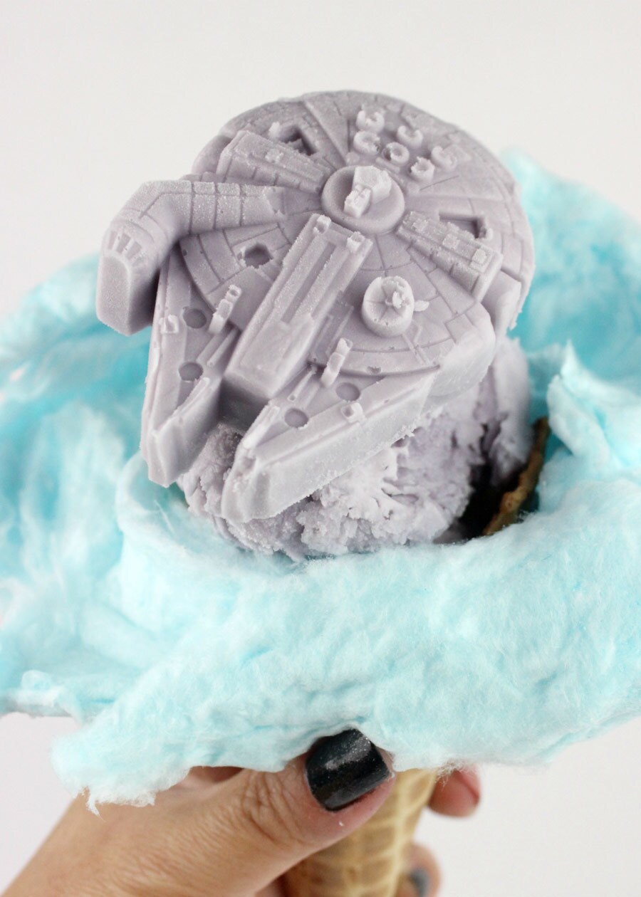 A Millennium Falcon-shaped ice cream scoop sits atop a cloud of blue cotton candy in a waffle cone.